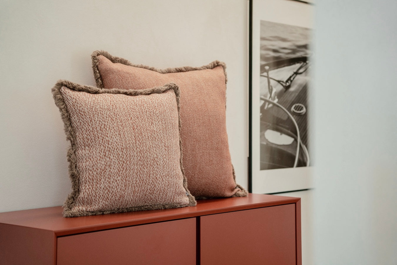 Zwei strukturierte indoor-Dekokissen in warmen Beige mit Fransen, arrangiert auf einer modernen Holzkommode als Interior-Lifestyle-Szene