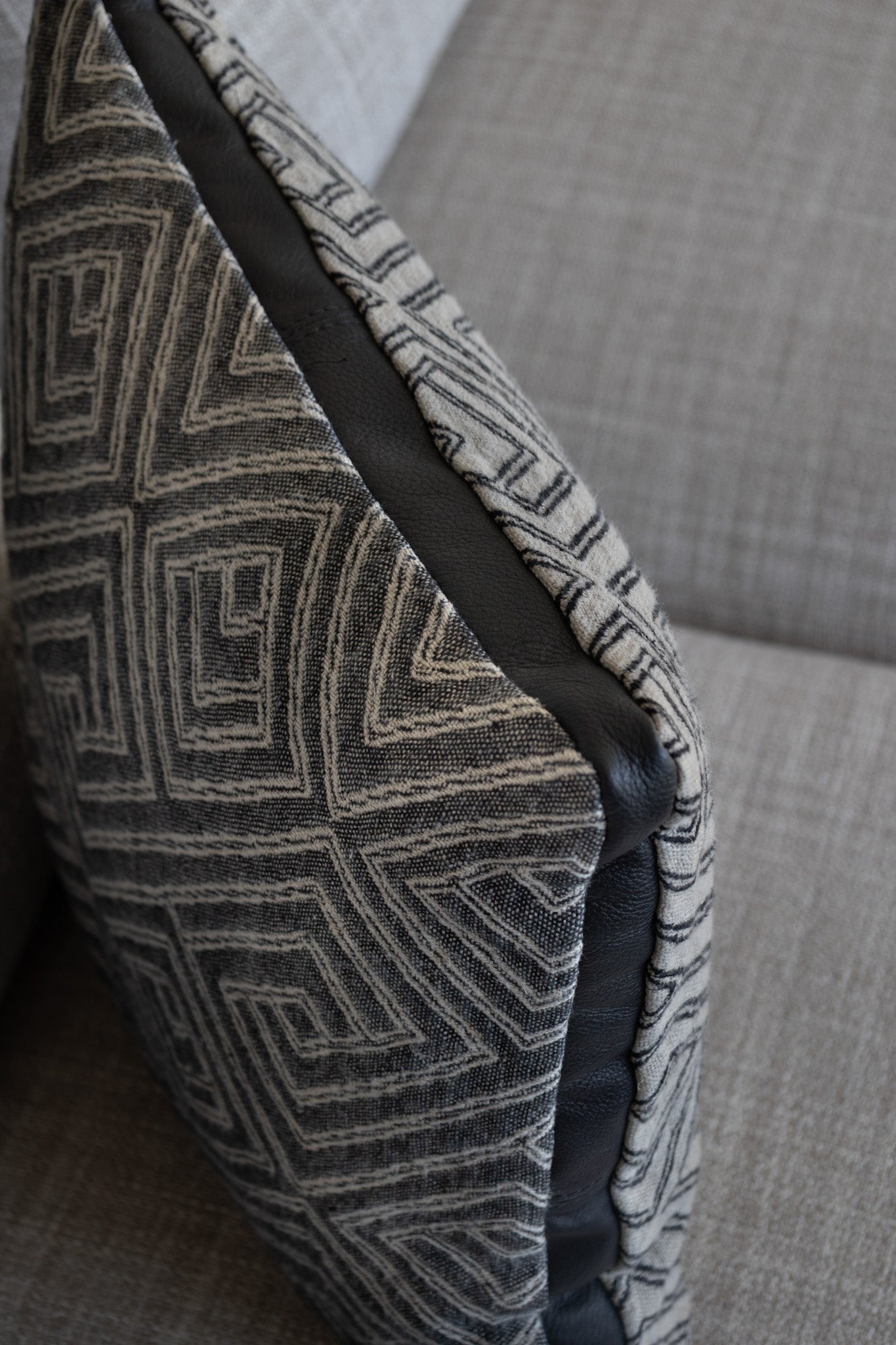Martin Gabriel Dekokissen Modell Noir Labyritnh schräge perspetive sichtabr vorder rücksoete grau scharzes leinen mit design streifen labyrith und bordüre mittig in leder schwarz auf sofa beige grau 