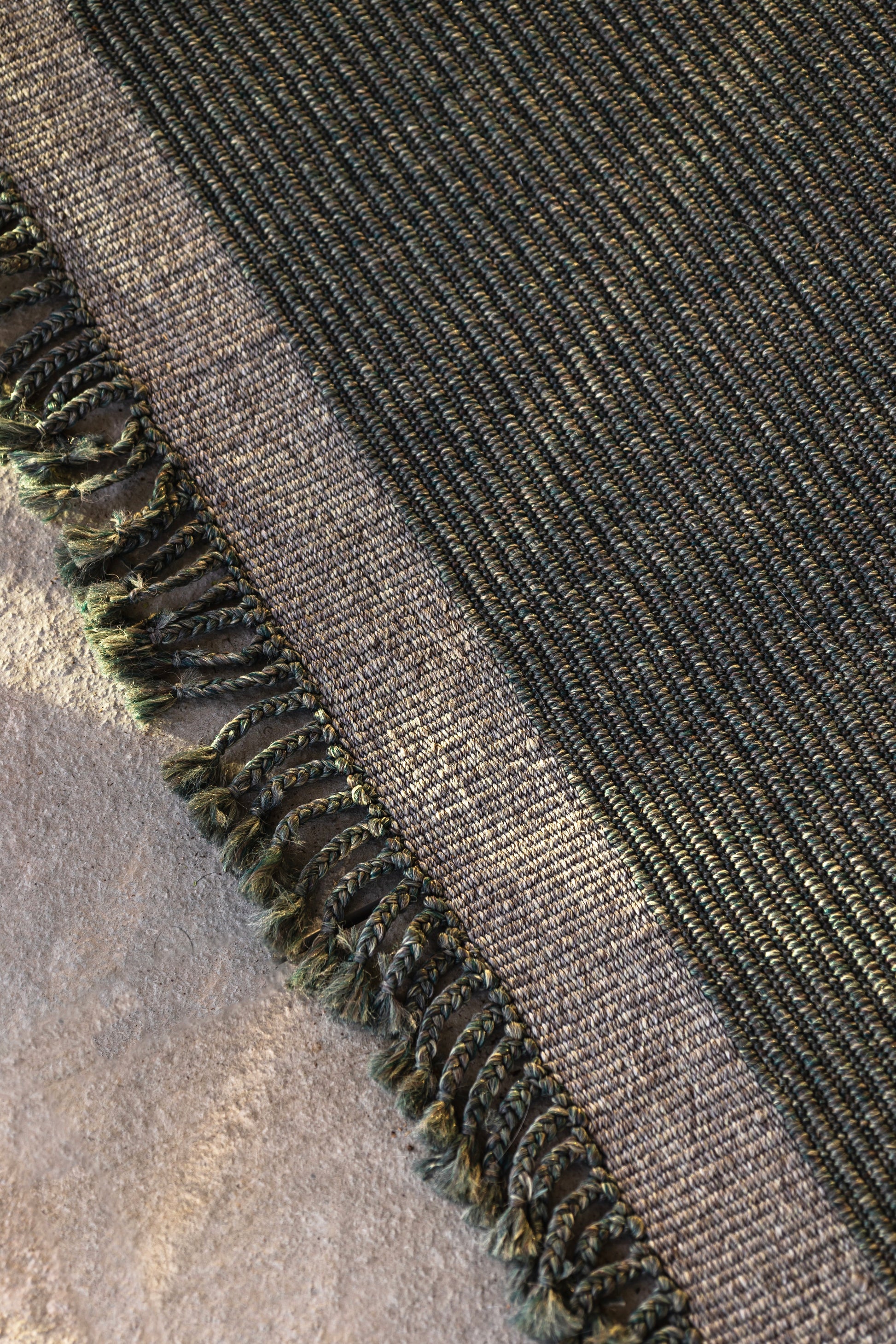 detailaufnahme outdoor teppich in einem grün grau mit fransen auf steinboden 
