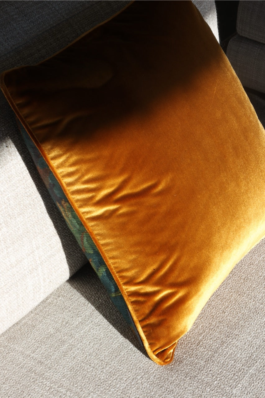 Martin Gabriel Designkissen modell schwarzwald , rücksiete in goldigen samtvelour und selbigen keder auf einem sandfarbenen sofa 