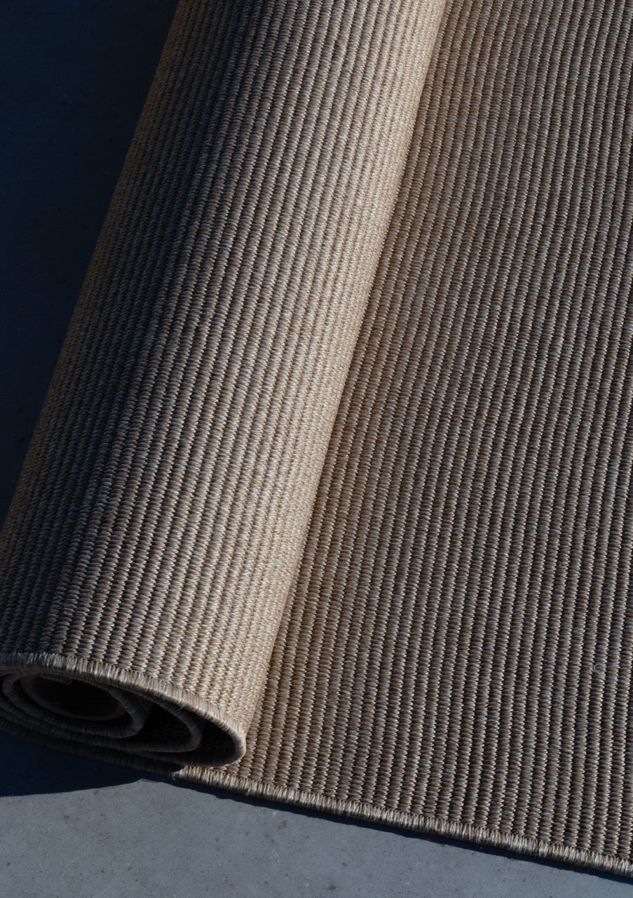 Outdoor Teppich zusammen gerollt als detail aufnahme auf steinboden in taupe sand mit struktur martin gabriel