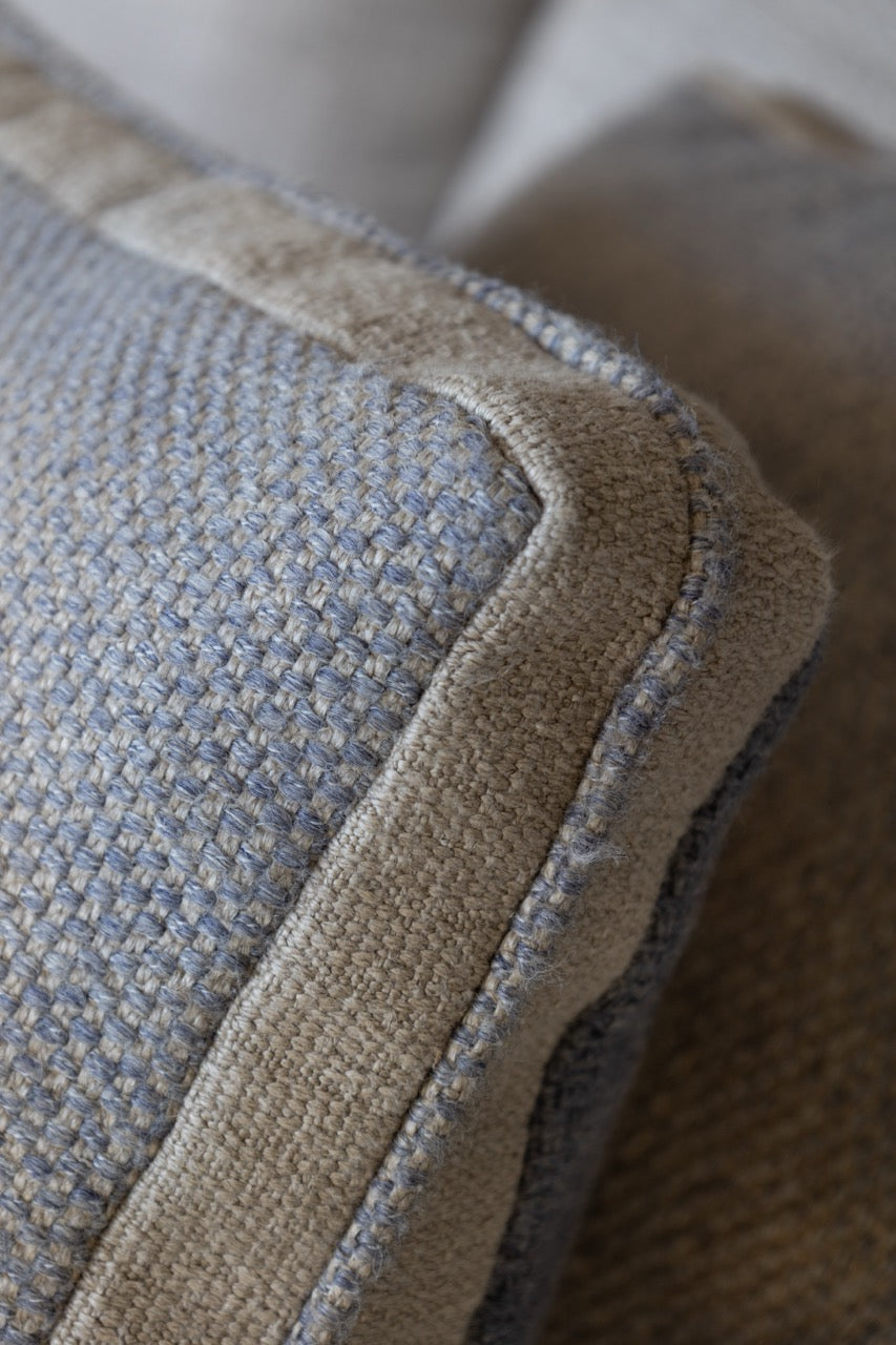 Martin Gabriel Dekokissen Modell Blue wave Calm nahaufnahme blaugraues leinen mit einer beigen bordüre und ein mittlekeder in blau seitlich sichtbar auf sofa