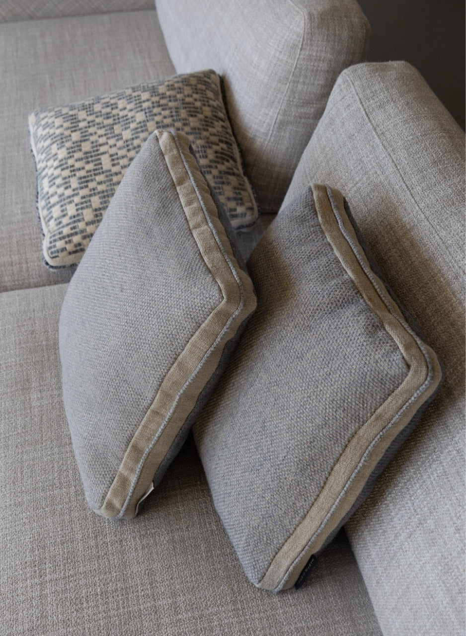 Martin Gabriel Dekokissen Modell Blue Wave Calm in taubenblauem leinen mit beigen akzenten auf sofa zusamme mit zwei weiteren kissen aus der sekben farbfamilie auf beigem sofa seitenansicht