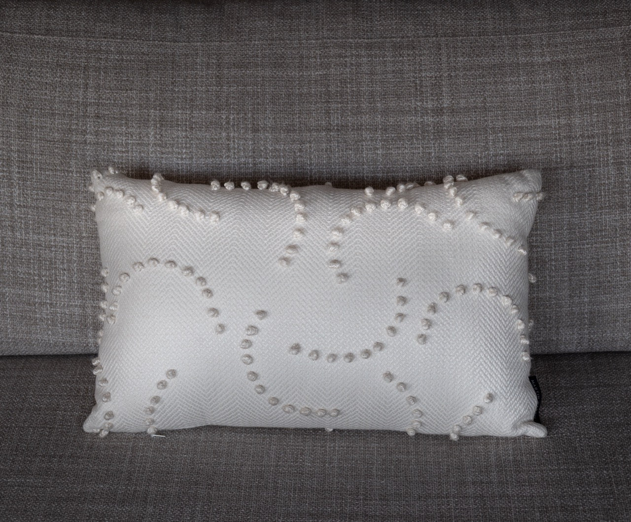 Martin Gabriel Dekokissen Model Soft Relief White in 40 x 60 cm auf sofa in wiess mit kleinen kügelchen in einen hab kreis wiederholend auf beigem sofa 
