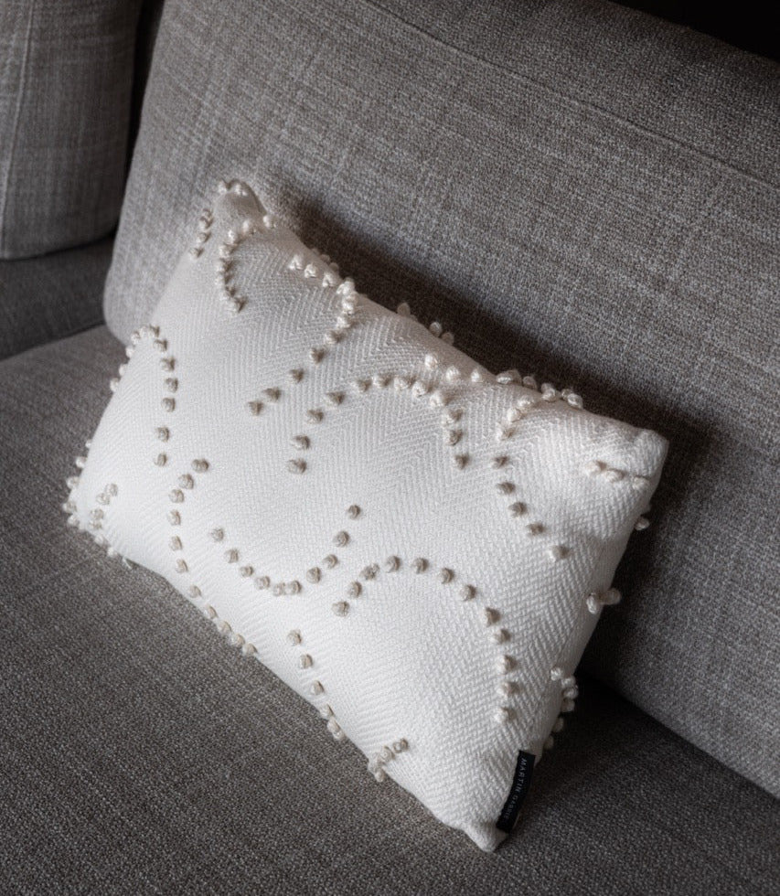 Martin Gabriel Zierkissen Modell Soft relief white auf sofa in schräger ansicht von der seite in weiss mit pajetten in wolle auf beige grauem sofa 