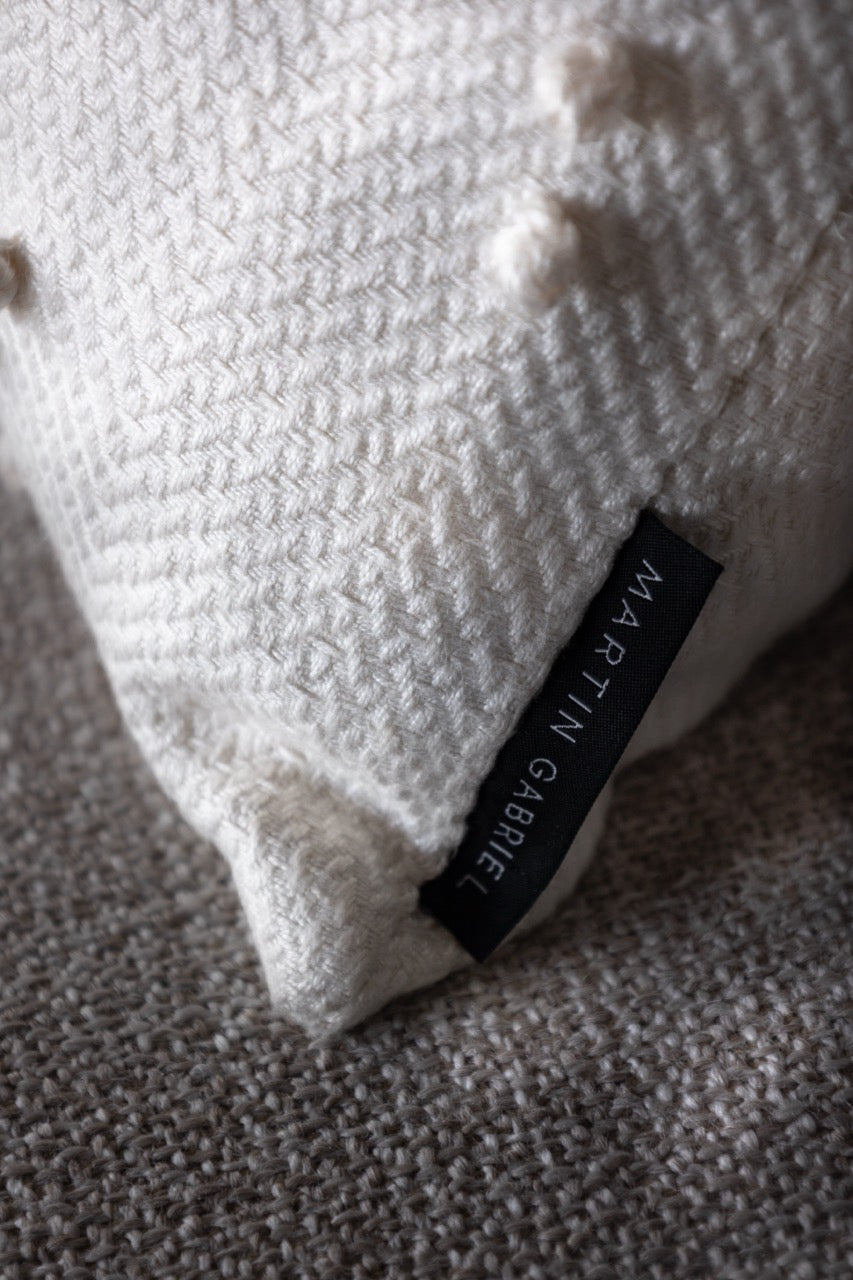 Martin Gabriel Zierkissen detailafnahme label mit namen und struktuer weisses textil auf beigem textil untergrund 