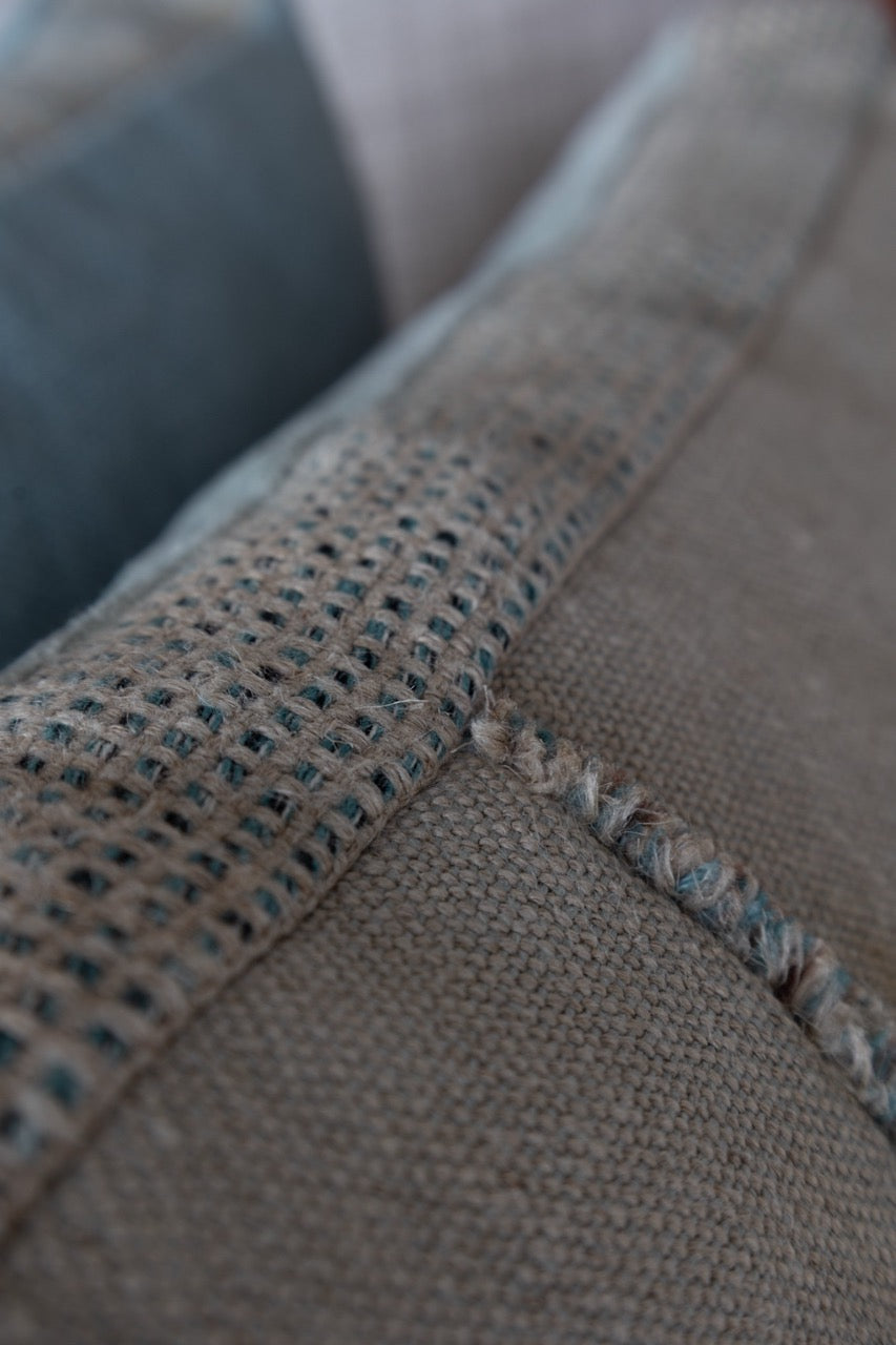 Martin-Gabriel Leinen Dekokissen Blue Ligne 02 mit Mittelband und feiner Fransenkante in Naturton und hellblauer Rückseite auf Sofa detailansicht
