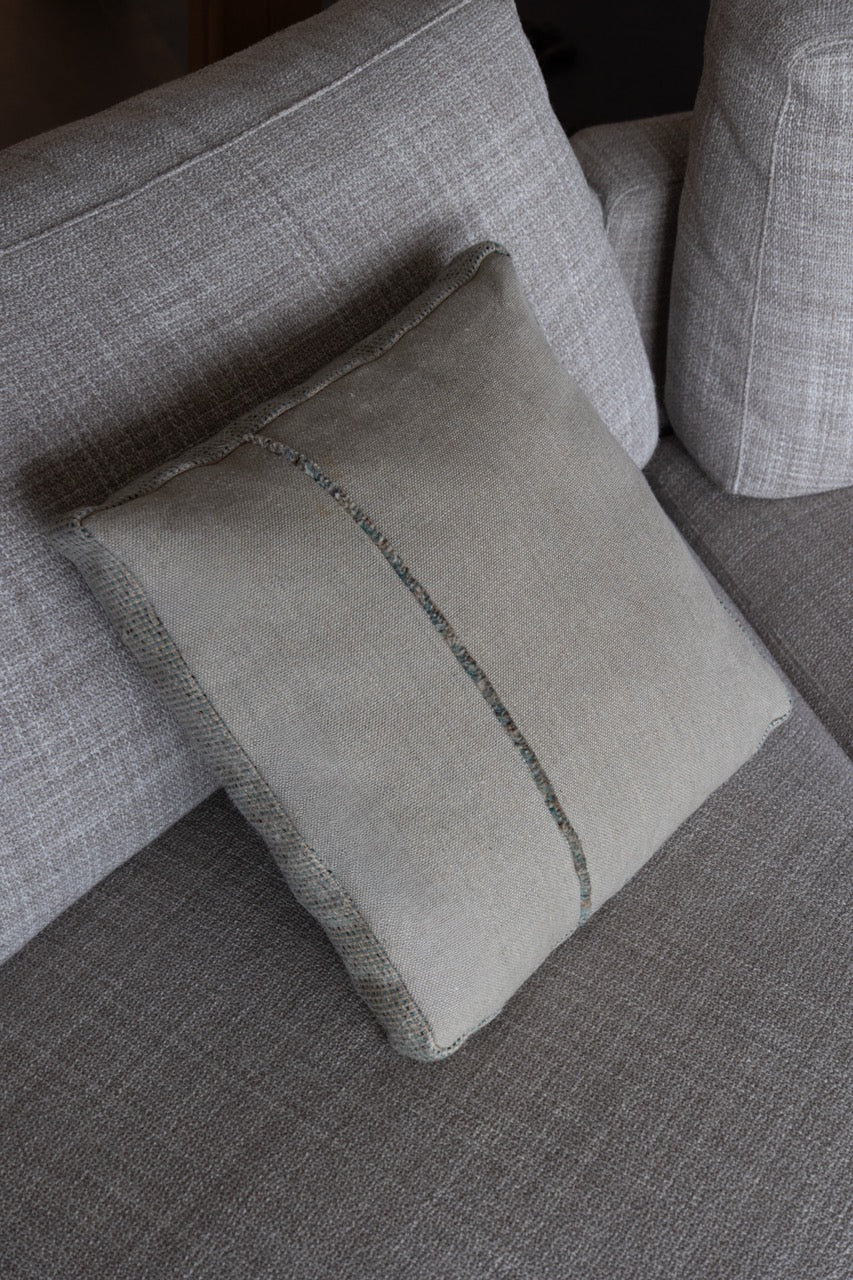 Martin-Gabriel Leinen Dekokissen Blue Ligne 02 mit Mittelband und feiner Fransenkante in Naturton und hellblauer Rückseite auf Sofa
