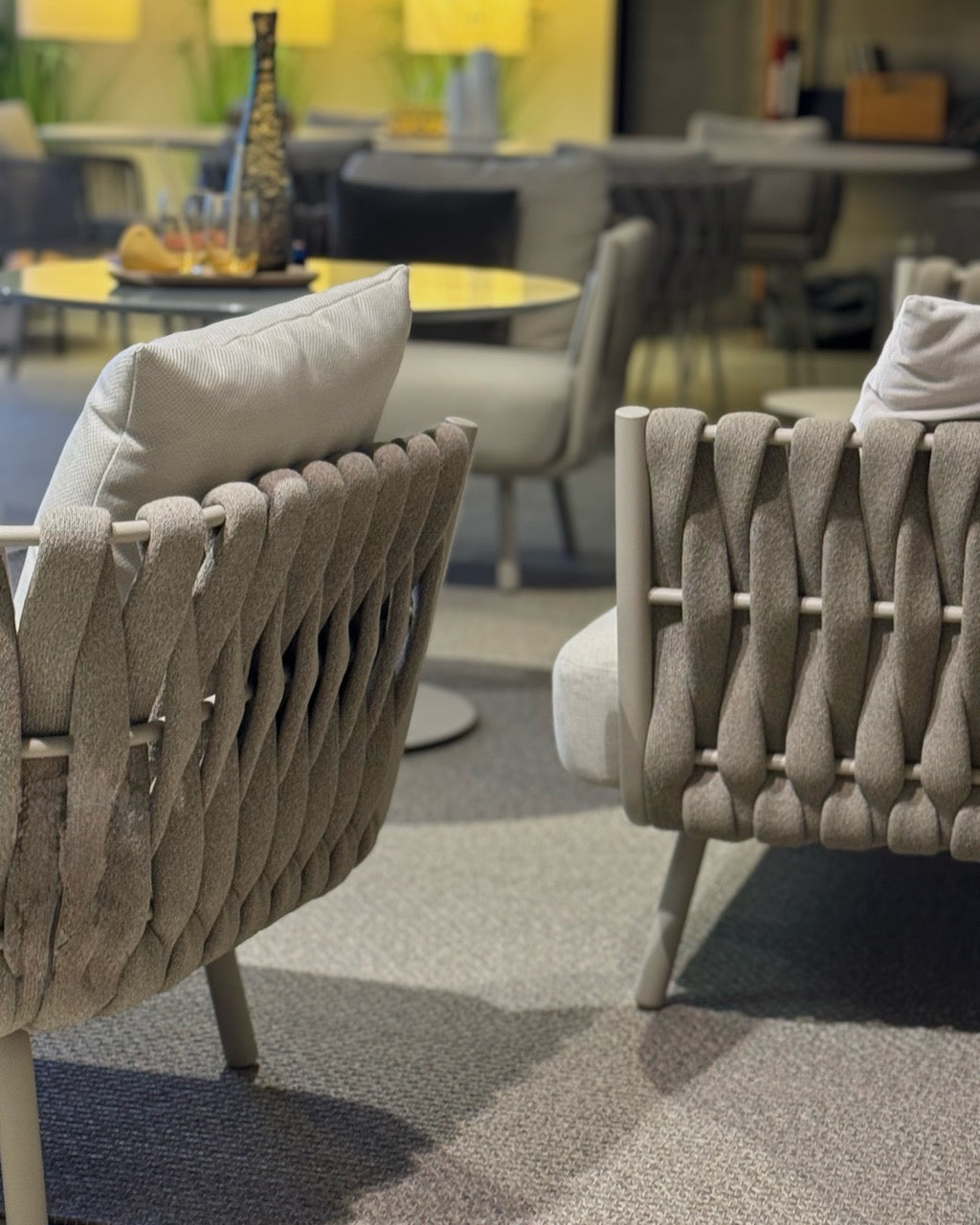 Detailaufnahme eines modernen Lounge-Bereichs mit geflochtenen Sessellehnen und weichen Polstern in neutralen Farbtönen. 
