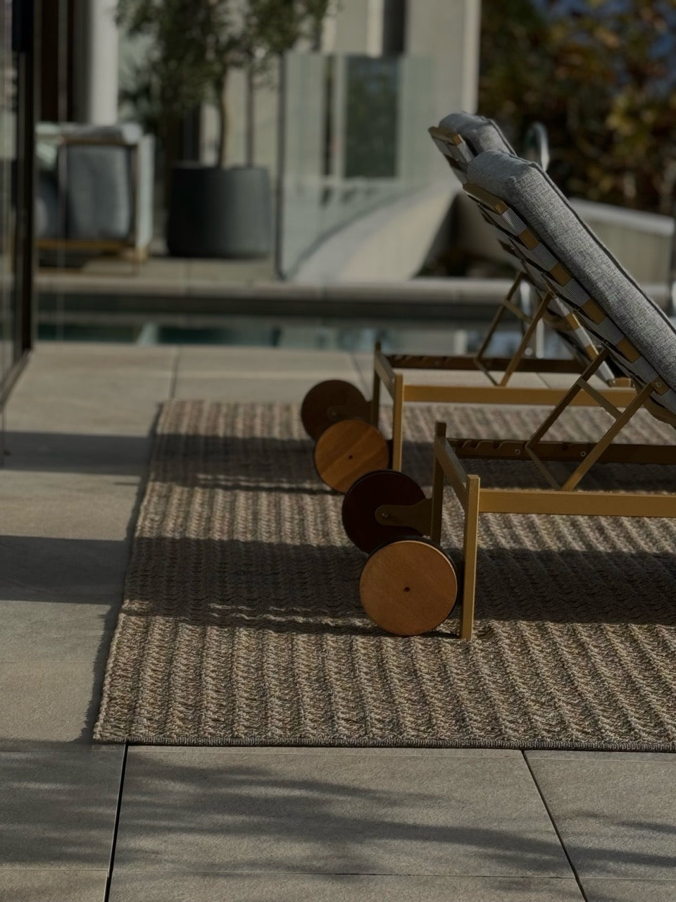 Outdoor-Liegestuhl auf moderner Terrasse, kobiniert mit zwei Martin-Gabriel-Outdoor-Teppichen in warmen Naturtönen.