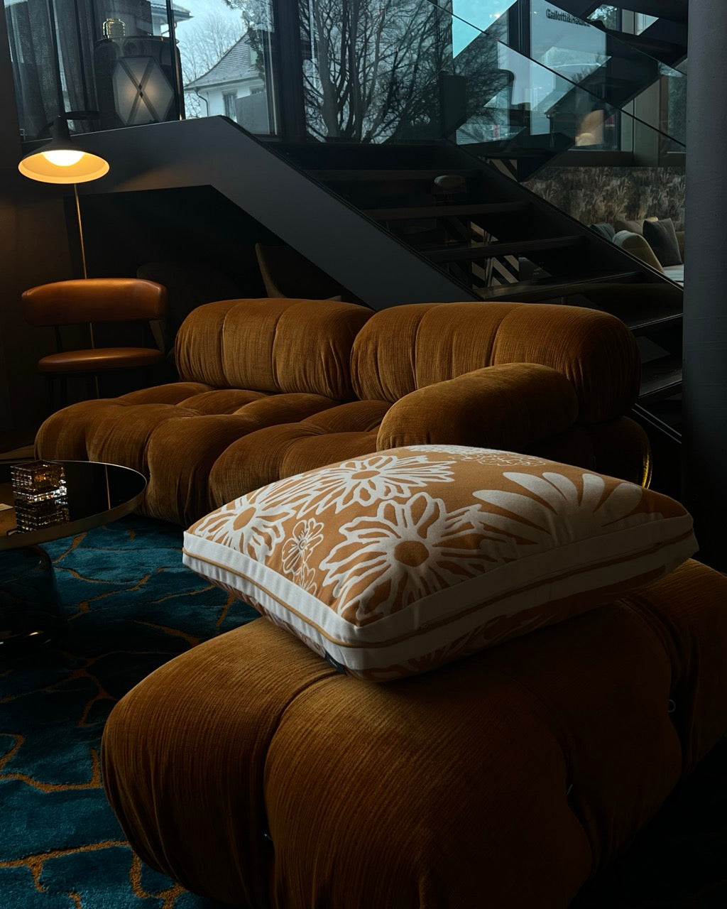 Samtiges Lounge-Sofa in warmen Braunton mit dekorativem Martin-Gabriel-Kissen im floralen Muster. 