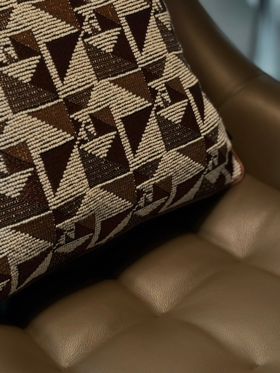 Martin Gabriel designkissen modell Geometrie auf braunem ledersessel mit chesterfield look und da kissen mit geometrischen design in der selben farbfamilie 