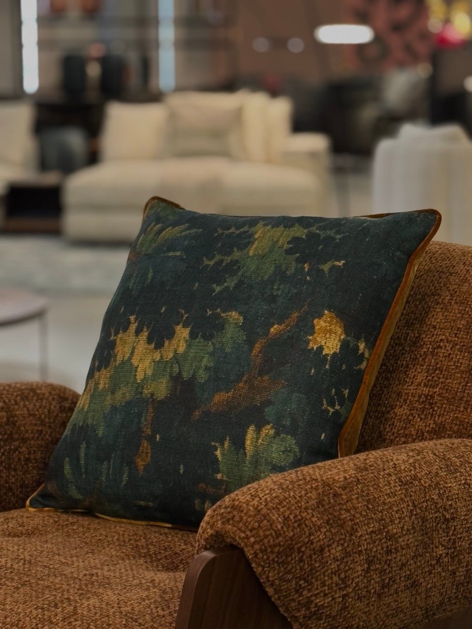 Martin Gabriel Desihnkissen modell schwarzwald auf rostbraunem sessel liegend in goldigen Farben in showroom 