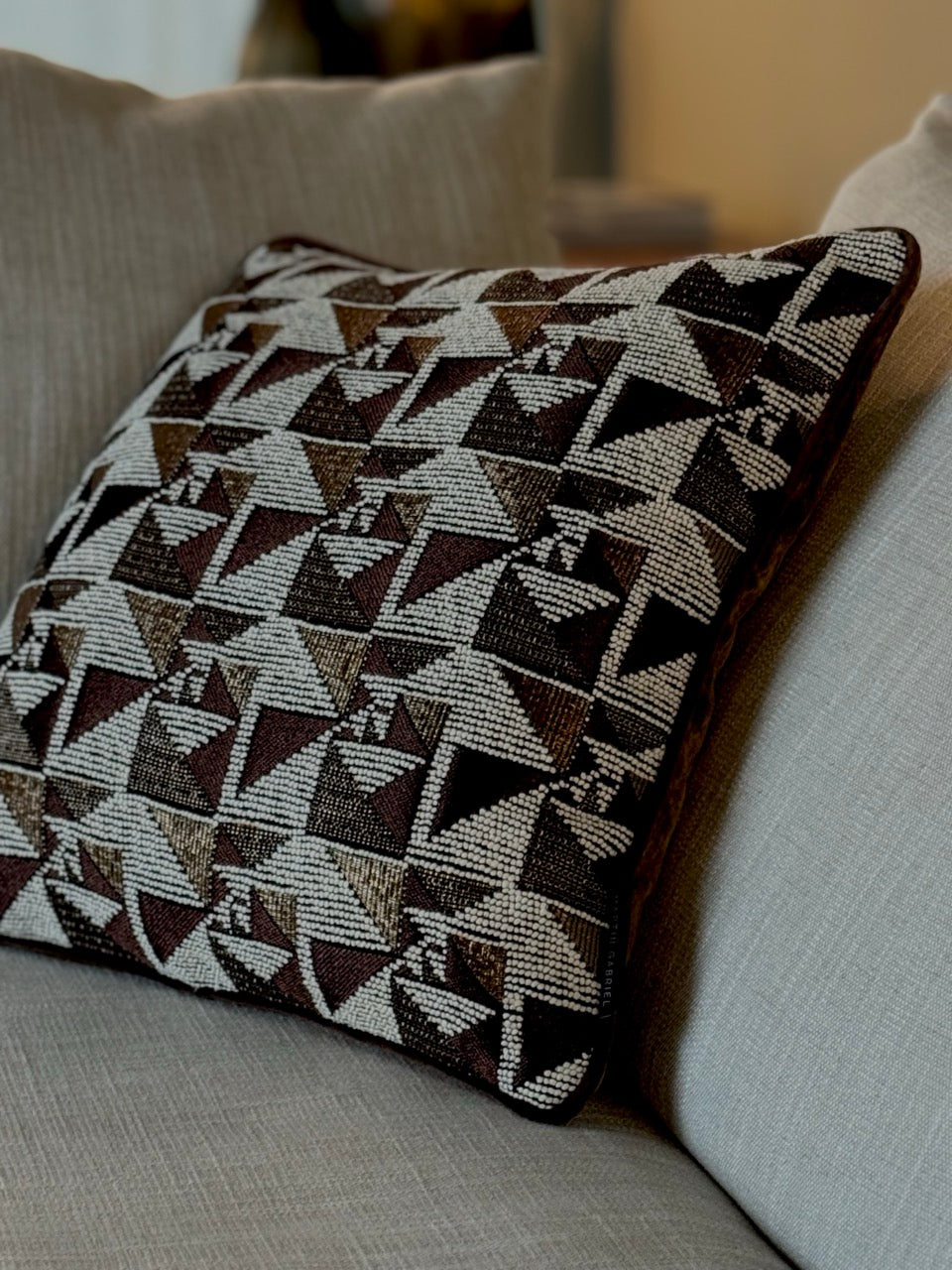 Martin Gabriel Designkissen Modell geometrie in braun gold bronzenen mit weiss gemusterten Design auf einem beigen sofa 