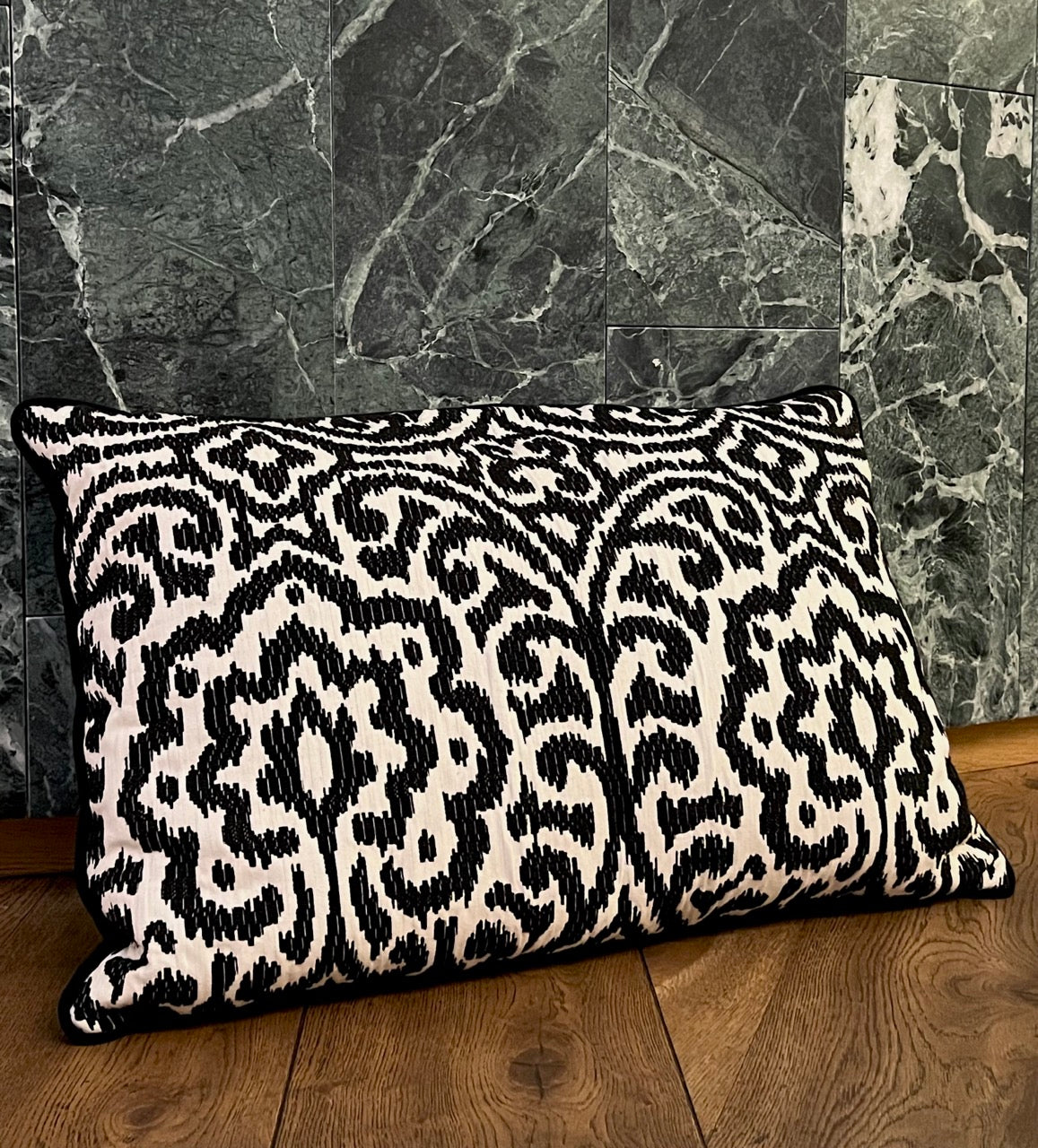 Martin Gabriel Designkissen Modell Relief Noir schwarz weisse relief struktur mit ornament muster auf holzboden und grünen marmor an der wand 