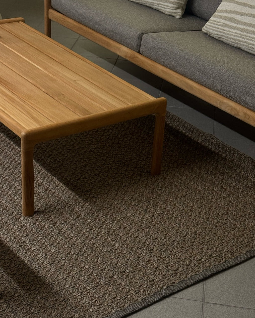 Wohnbereich mit Holz-Couch-tisch und Sofa, kombiniert mit einem strukturerten Martin-Gabriel-Outdoor-Teppich in warmen Naturtönen.