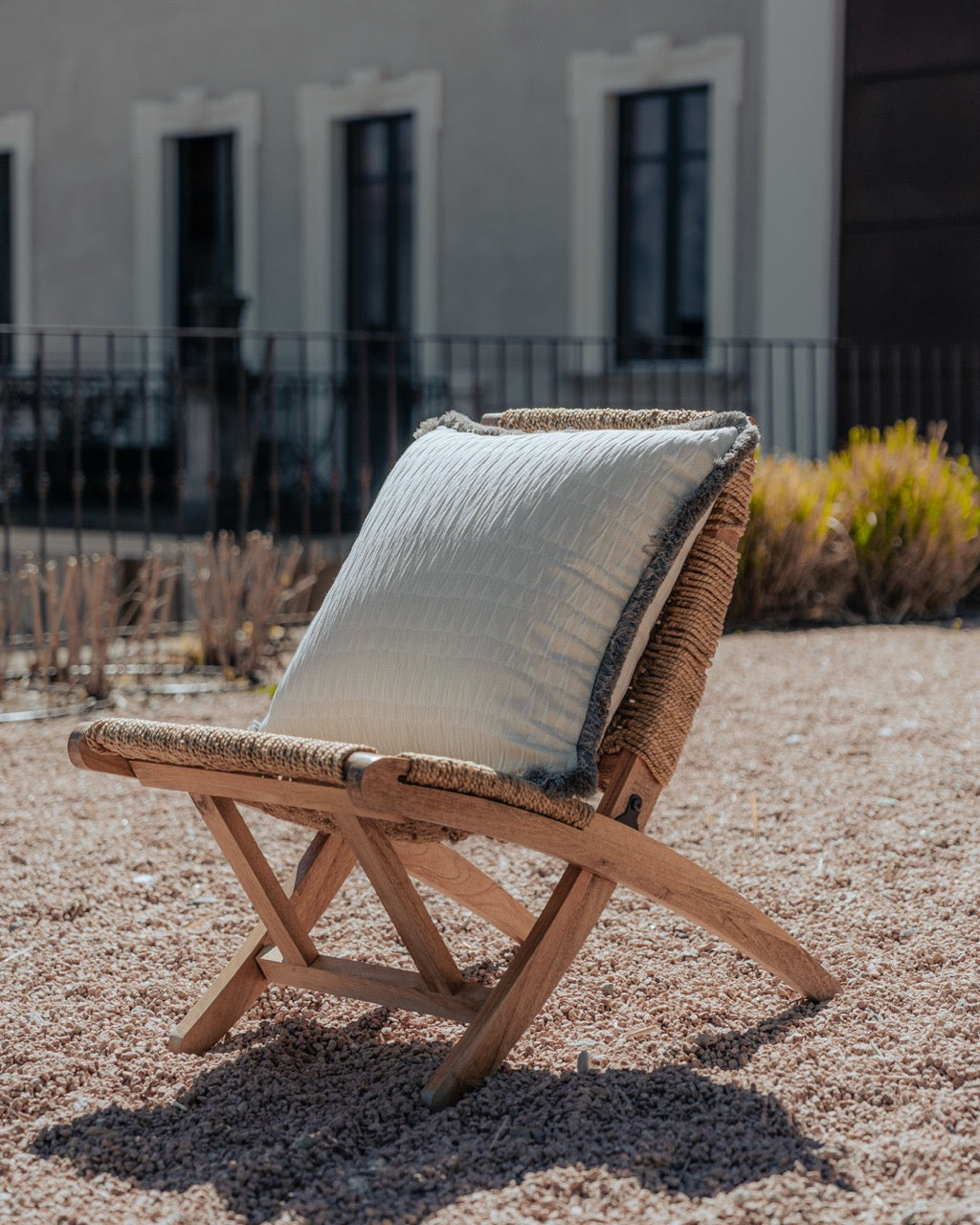 helles Outdoor Kissen mit Fransen auf sessel auf grosser terrasse mit kies