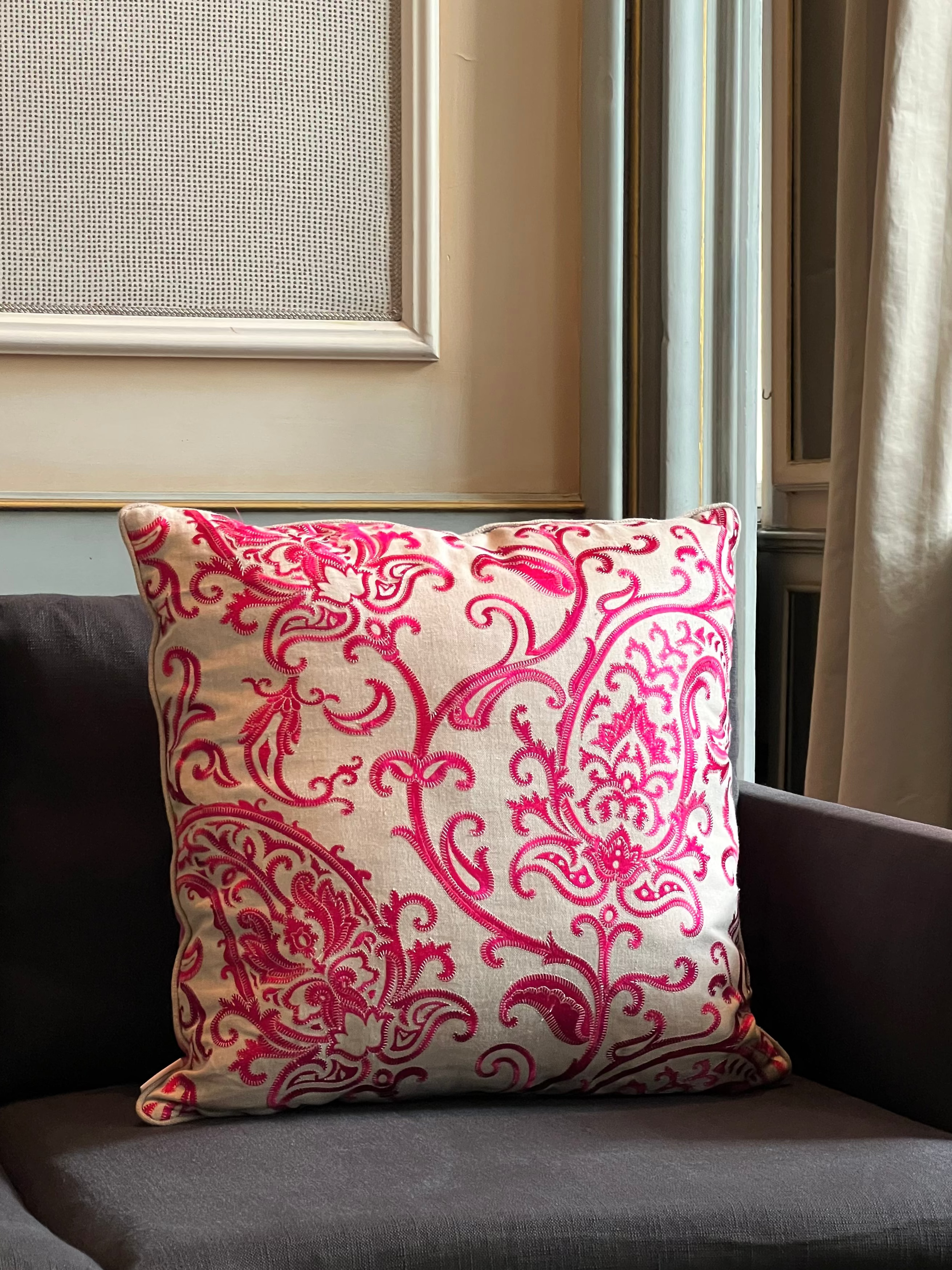 Martin Gabriel Deko-Kissen aus besticktem Muster in Magenta pink mit ornamentalem Muster auf Naturgrund, seitliche Garnverarbeitung, inszeniert auf Polstermöbel