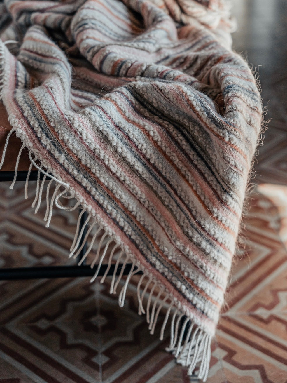 Gestreifte Wohndecke mit Fransen, drapiert über einer Oberfläche, in warmen Naturtönen 