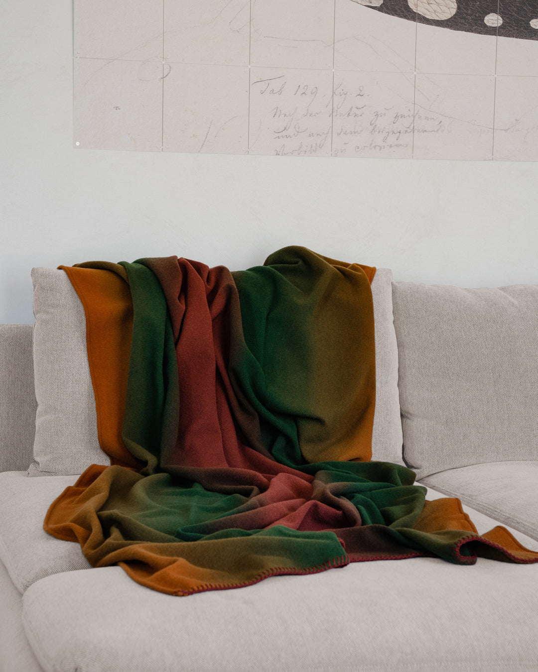 Martin Gabriel Plaid Modell shadow in farbverlauf orange, grün, rostrot auf sofa in beige 