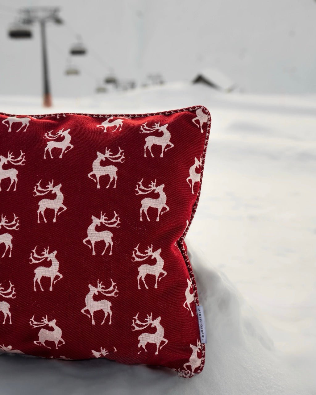 Martin Gabriel Indoor Kissen Chalet Kollektion Modell Alpine Redstag in rot mit weissem Hirschmotiv im schnee mit Gondel i Hintergrund stimmungsbild 