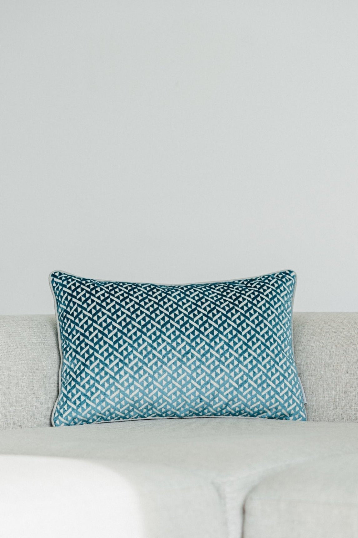 Martin Gabriel deko Kissen Modell azzurro mit hellblauen kleinen dreiecken aus velour und auf hellgrauer wolle auf einem hellgrauem sofa 