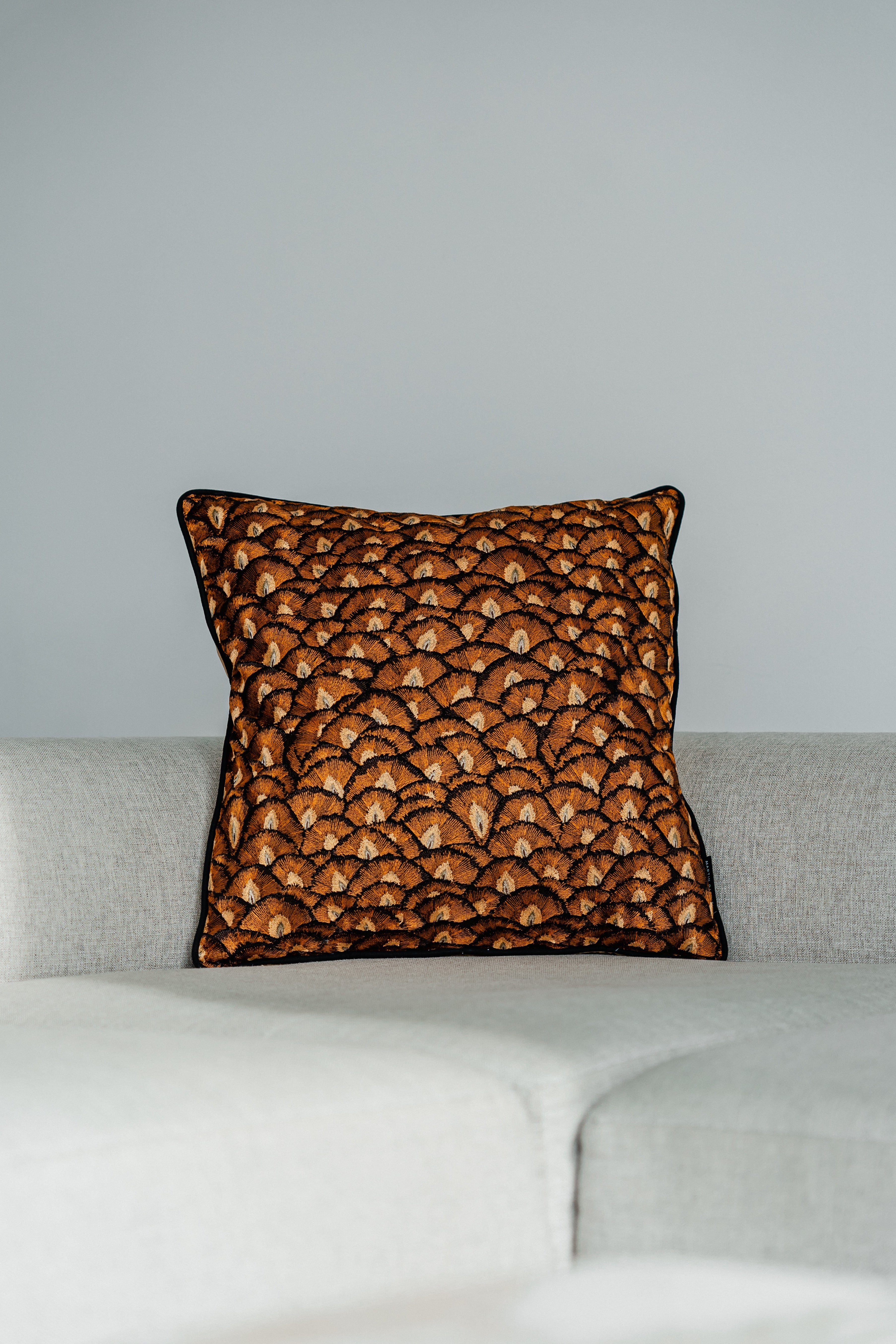 Quadratisches Deko-Kissen 60x60 cm mit bestickter Vorderseite in Braun- und Karamelltönen auf hellem Sofa