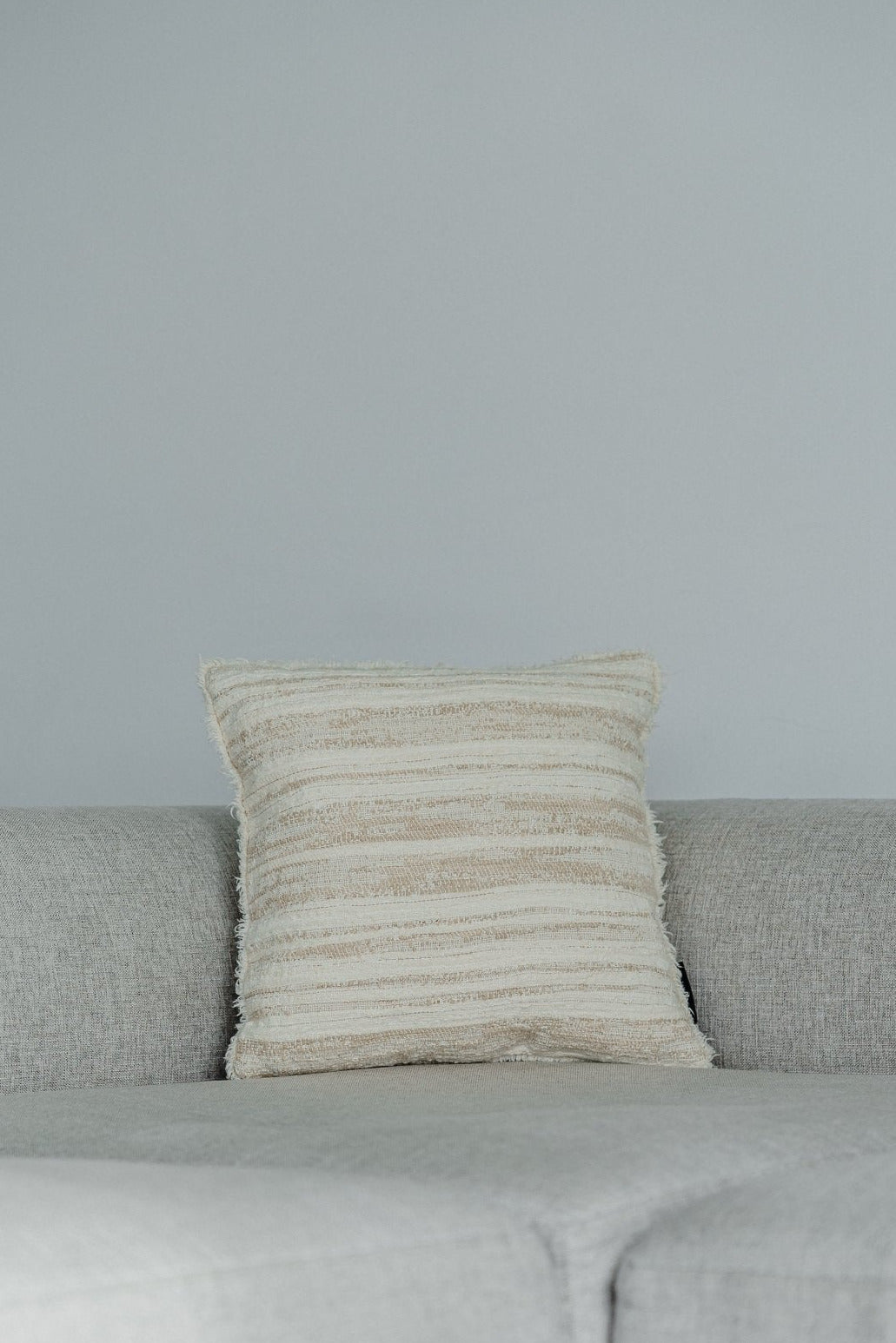 Martin Gabriel Deko Kissen modell Livorno aus strukturierter Naturtextilie mit horizontalen Streifen in beige und Naturtönen auf grauem Sofa