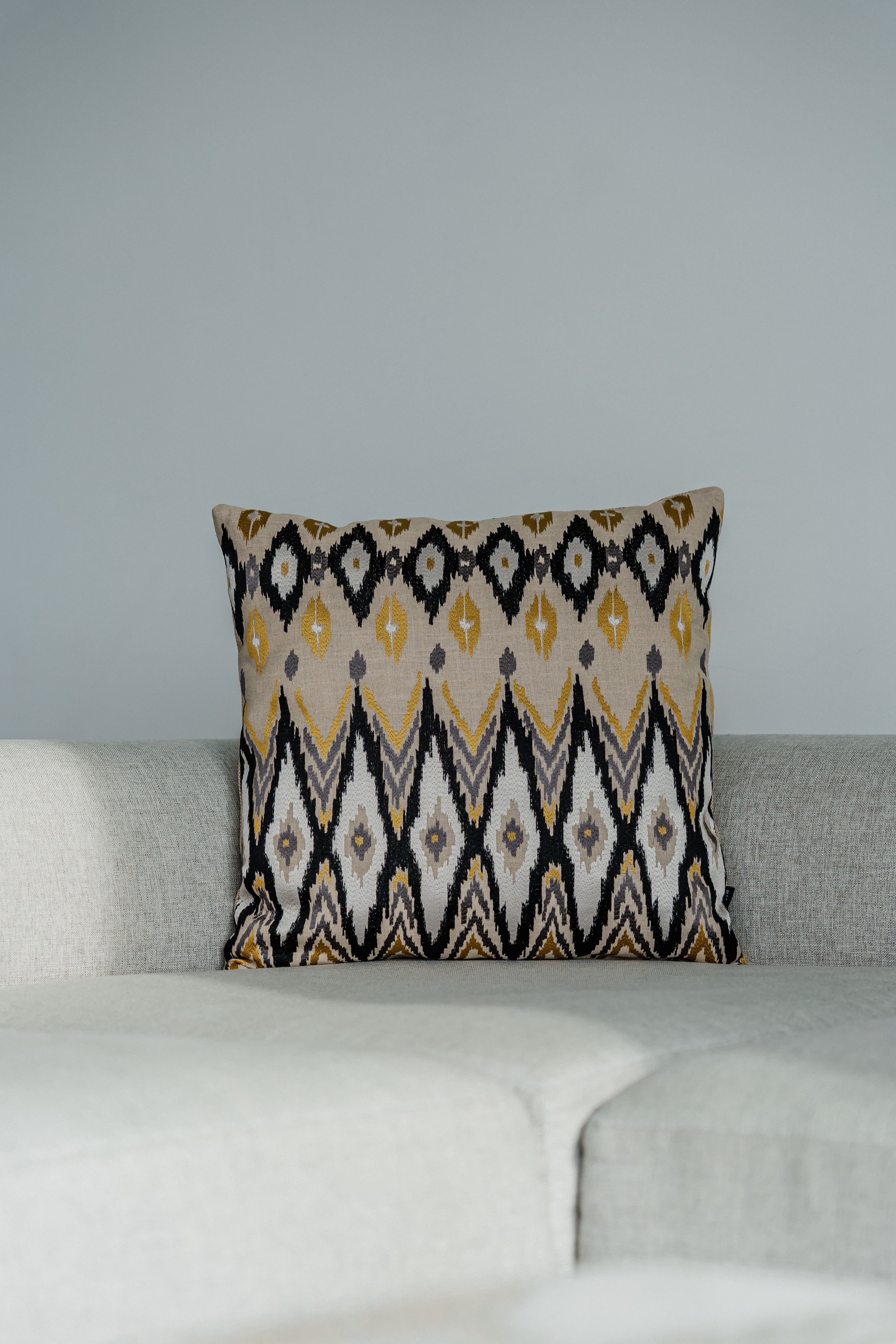 Designer-Dekokissen im Ikato-Muster in Beige, Gelb und Schwarz von Martin Gabriel, dekoriert auf hellem Sofa im Wohnzimmer.
