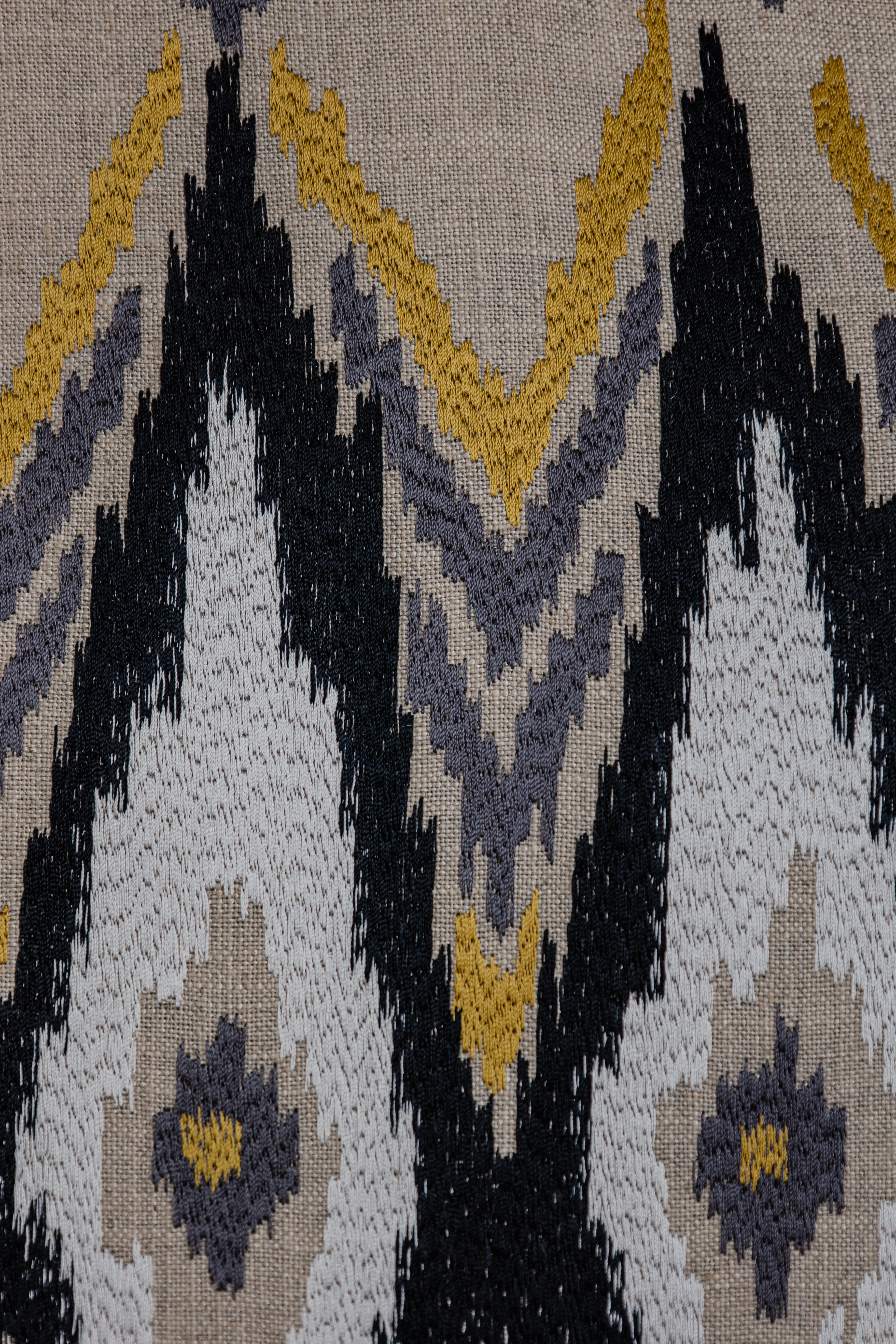 Detailaufnahme der Stickerei des Ikato-Kissens in Beige, Gelb, Grau und Schwarz, hochwertige Textilstruktur.
