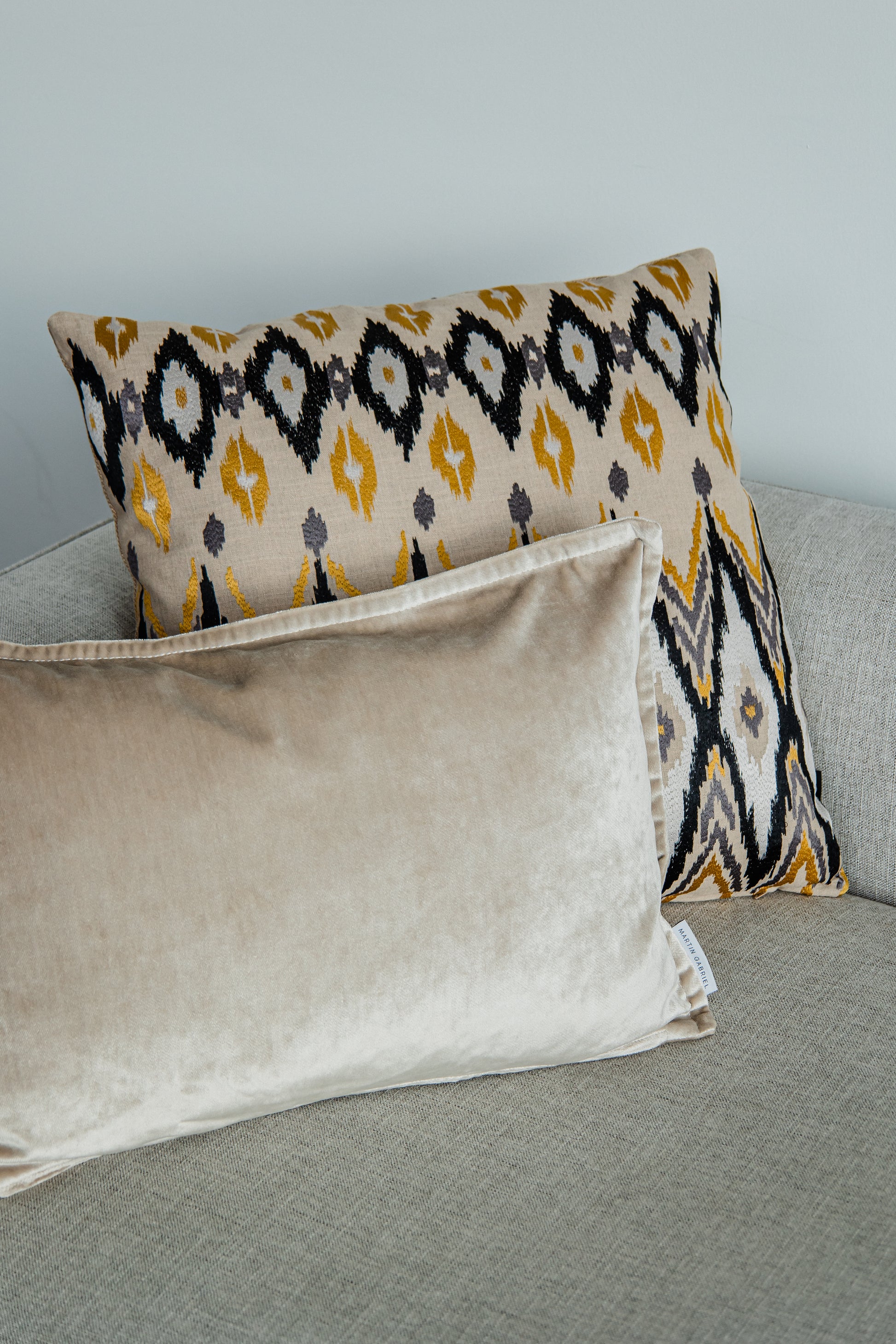 Dekokissen im Ikato-Design in Beige, Gelb und Schwarz von Martin Gabriel, auf Sofa kombiniert mit beigem Samtkissen.

