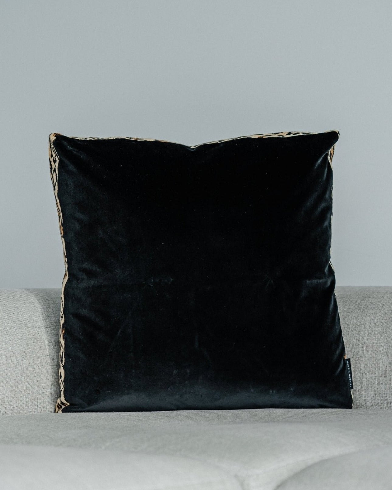 Martin Gabriel Designkissen Modell Leopard Noir auf einem grauen sofa in Fronansicht schwarzer velour vor weisser wand 