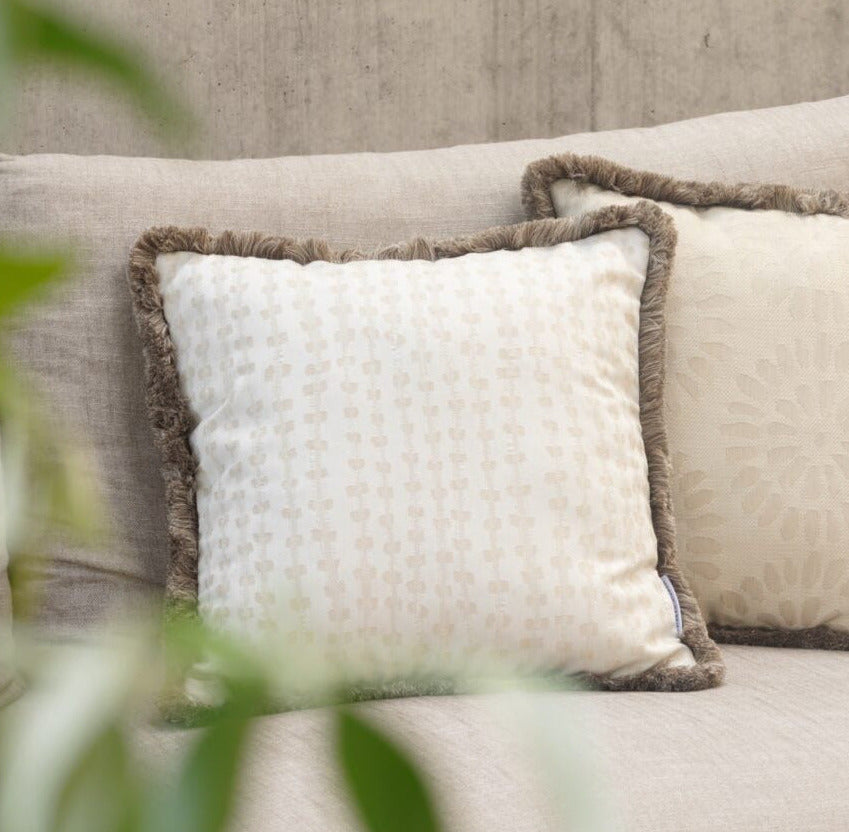 Outdoor Kissen  mit Fransen auf einem Sofa auf einer Terrasse in beigetönen mit einem weietren Kissen in dem selben farbton 