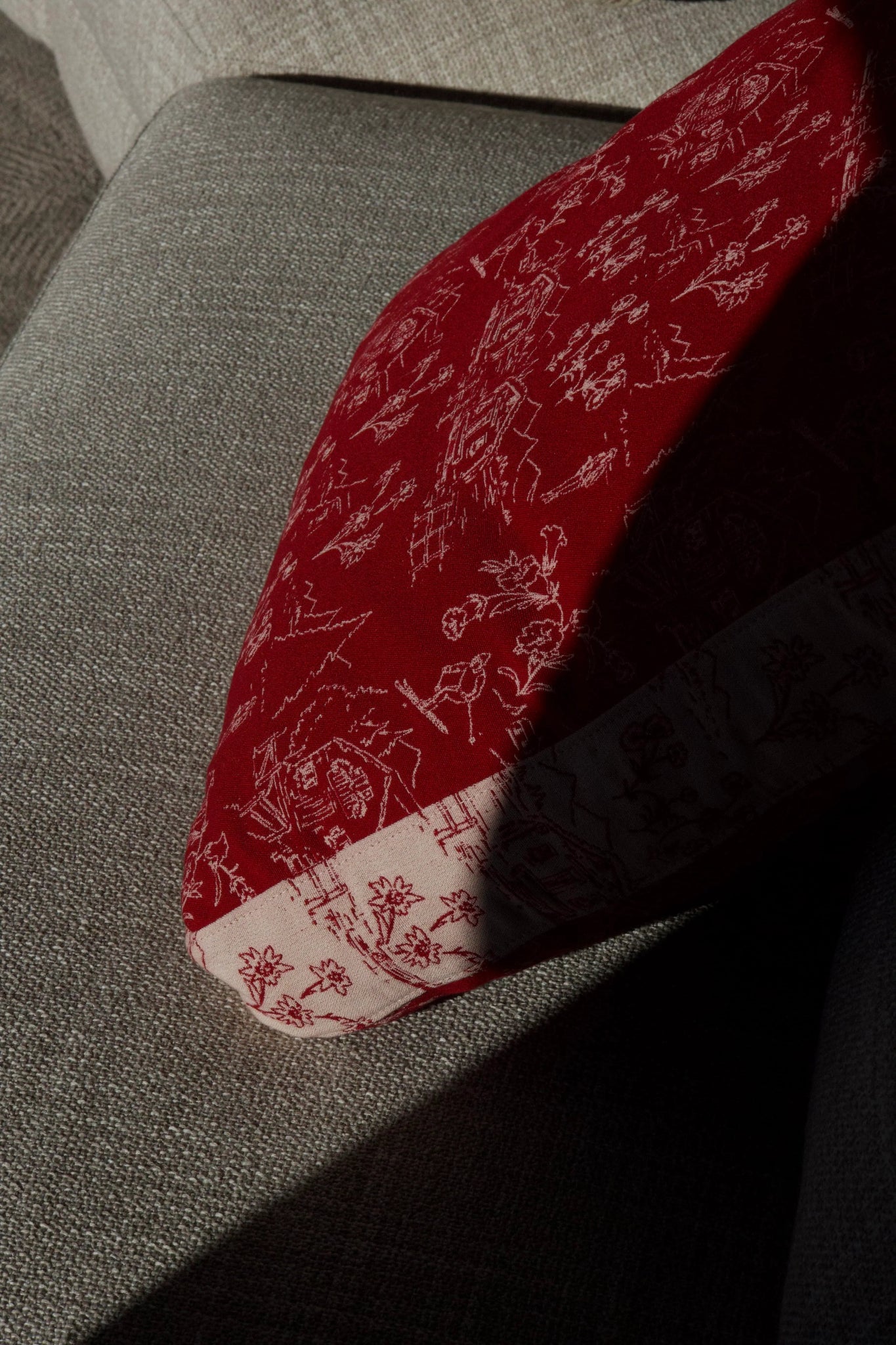Martin Gabriel Indoor Kissen Modell rouge panorama in rot mit weißem hüttenzauber und weißer bordüre mit roten muster als seitenasicht auf einem sofa im schatten 