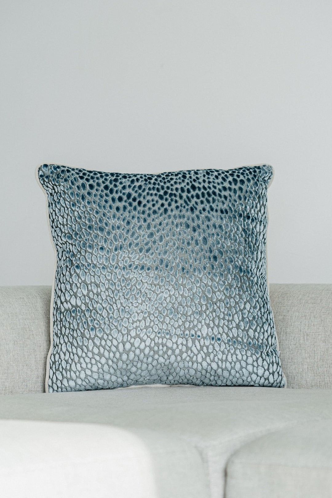 Martin Gabriel Deko Kissen Modell Dop in einem Blau silber grauen deisgn aus Velour Jacquard und einen hellgrauen keder aus Velour auf einem hellgruaen sofa